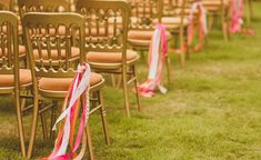 rows of chairs with ribbons on them in the grass at an outdoor wedding ceremony,