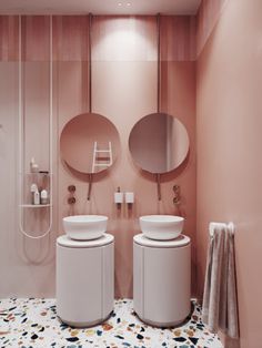 a bathroom with pink walls and two round mirrors on the wall, along with white pedestal sinks