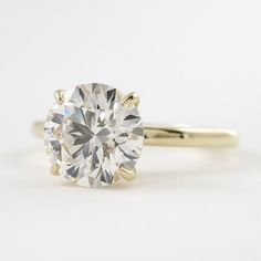 a yellow gold engagement ring with a round brilliant cut diamond in the center, on a white background