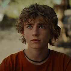 a close up of a person wearing an orange shirt and looking at the camera with a serious look on his face