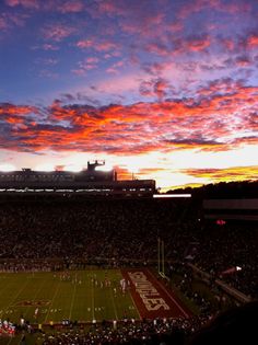 the sun sets over a football stadium as it is lit up with red and purple clouds