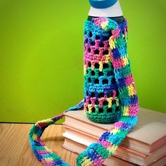 a colorful crocheted water bottle cover sitting on top of a stack of books