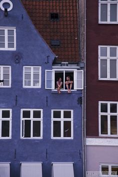 two people are sitting in the windows of a blue house