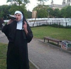 a nun drinking from a bottle while standing on the side walk in front of a park