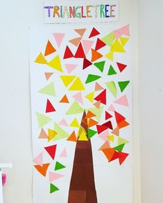 a tree made out of colored paper sitting on top of a white table next to a wall