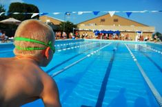 a young boy with green goggles on his head looking at an empty swimming pool