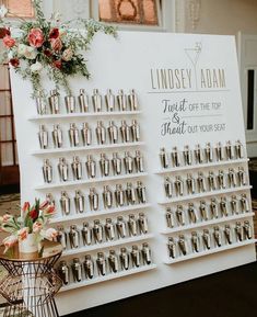 a table with an assortment of wedding rings on it and flowers in vases next to the sign