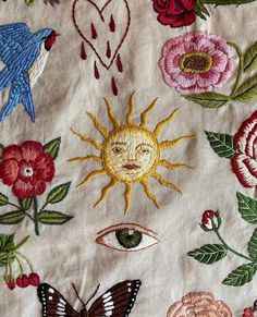 an embroidered fabric with flowers, birds and sun on it's side is shown