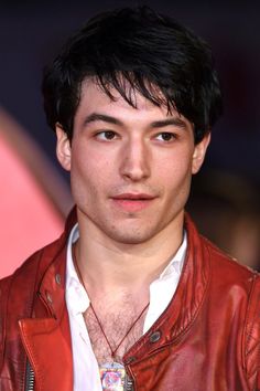 a man with black hair wearing a red leather jacket and white shirt is looking at the camera