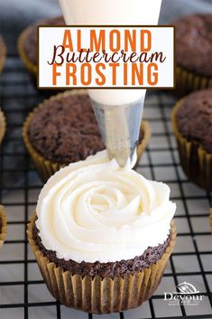 a cupcake being frosted with icing on a cooling rack next to other cupcakes