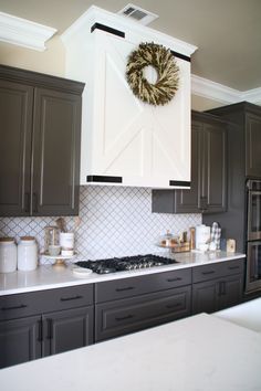 a kitchen with gray cabinets and white counter tops, wreath on the wall above the stove