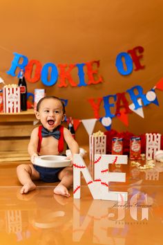 a baby is sitting on the floor with a bowl in front of him and decorations behind him