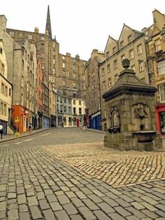 a cobblestone street in an old city with tall buildings on both sides and a clock tower at the end