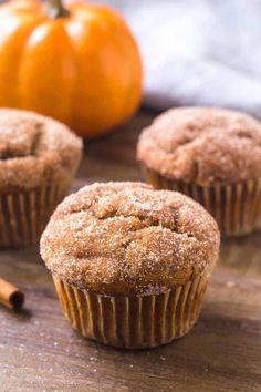 three cinnamon muffins sitting on top of a wooden table next to an orange pumpkin