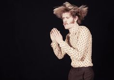 a man with his hair in the air and hands folded out, standing against a black background