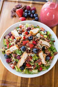 a salad with chicken, berries and blueberries in a white bowl on a wooden cutting board