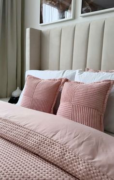 a bed with pink comforter and pillows in a bedroom next to two pictures on the wall