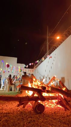 people sitting around a fire pit with flags hanging from the wall in the background at night