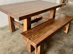 a wooden table and bench sitting in a room next to a brick wall on concrete flooring