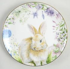 a plate with a painting of a rabbit on it's side and flowers in the background