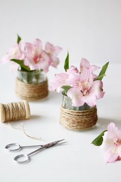 some pink flowers are in small vases with twine and scissors next to them