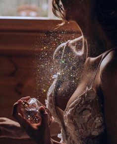 a woman is blowing glitter on her face and holding an object in her right hand