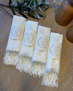 four white towels with labels on them sitting on a wooden table next to a vase