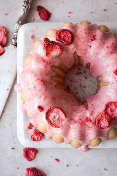 a cake with pink icing and raspberries on it next to a knife