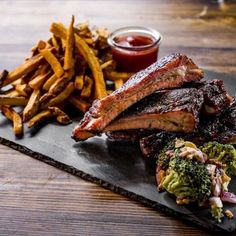 ribs, broccoli and french fries on a black plate with ketchup