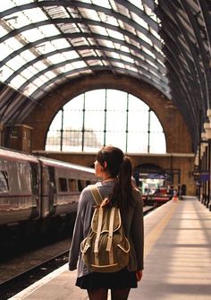 a woman with a backpack is waiting at the train station for her train to arrive