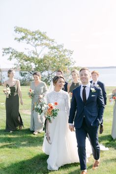 a bride and groom walking through the grass with their bridal party in the background