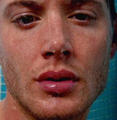 a close up of a man's face in front of a tiled wall with blue tiles