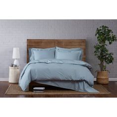 a bed with blue sheets and pillows in a room next to a potted plant