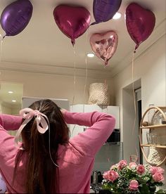 a woman in pink sweater holding up purple heart shaped balloons