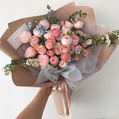 a bouquet of pink flowers is wrapped in brown paper and tied to a white wall