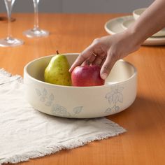 a person picking up an apple in a bowl on a table with wine glasses and napkins