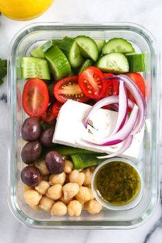 a salad in a plastic container with tomatoes, cucumbers, olives and cheese