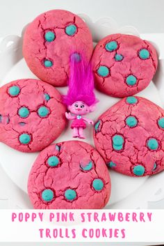 pink and blue cookies on a white plate with the words poppy pink strawberry trollies