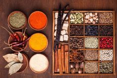 an assortment of spices and herbs displayed in wooden bowls on a brown table with spoons