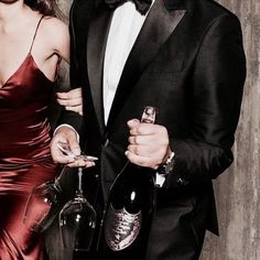 a man in a tuxedo and woman in a red dress holding wine glasses