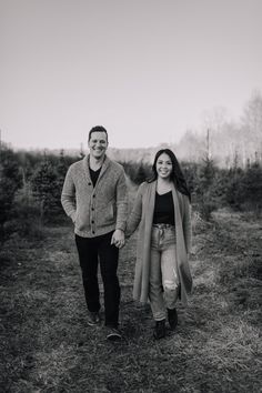 black and white photo of two people holding hands walking through an open field with trees in the background