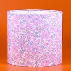 a pink and blue lamp shade with flowers on it, against an orange wall background