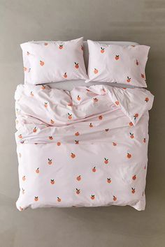 a bed with pink sheets and oranges printed on the comforter, along with two pillows