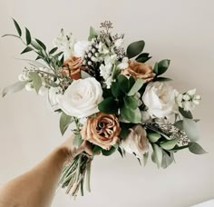 a bouquet of flowers being held by someone's hand in front of a white wall