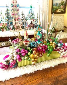 an arrangement of christmas ornaments in a green container on a table with white furnishing