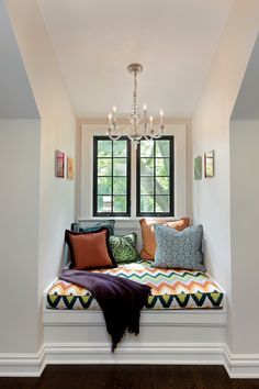 a window seat with pillows on it and a chandelier hanging from the ceiling