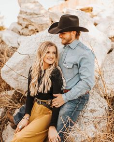 a man and woman sitting next to each other in front of rocks wearing cowboy hats