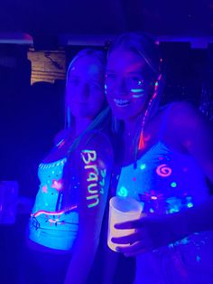 two young women standing next to each other in the dark with neon paint on their arms