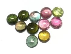 six different colored glass beads on a white surface, with one small hole in the middle