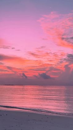 the sky is pink and purple as the sun sets over the ocean on an empty beach